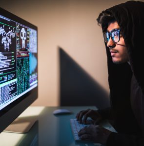 cybercrime, hacking and technology concept - male hacker with smartphone and coding on computers screen in dark room